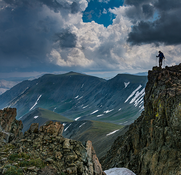 a person standing on a rocky cliff with mountains in the background